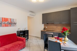 Una cocina moderna con armarios oscuros, encimera de madera y una zona de comedor con un sofá rojo y un florero.
