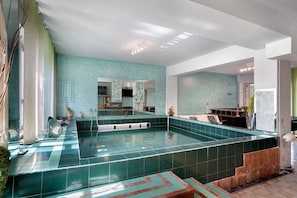 A spacious indoor swimming pool with a tiled floor and a large mirror reflecting the room.