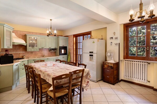 A kitchen with a dining table, chairs, a refrigerator, a stove, and a window with a view.