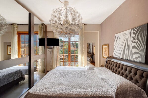 Un dormitorio con una cama grande, televisión, candelabro y obras de arte en las paredes.
