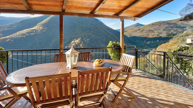 A wooden deck with a round table and chairs, overlooking a mountainous landscape.