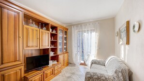 A living room with a TV, wooden cabinets, a sofa, and a window with curtains.