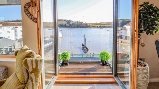 Un balcon avec vue sur un lac, un voilier et un paysage urbain au loin.