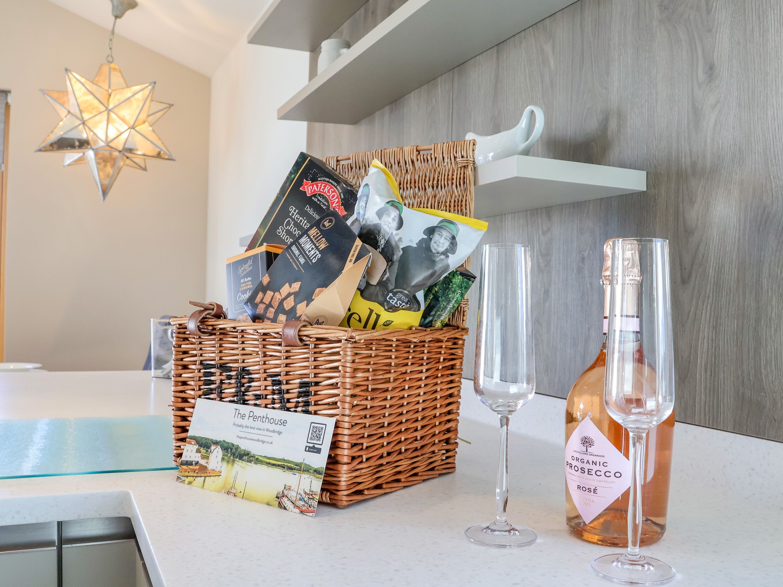 A wicker basket filled with books and a bottle of organic prosecco on a kitchen counter.