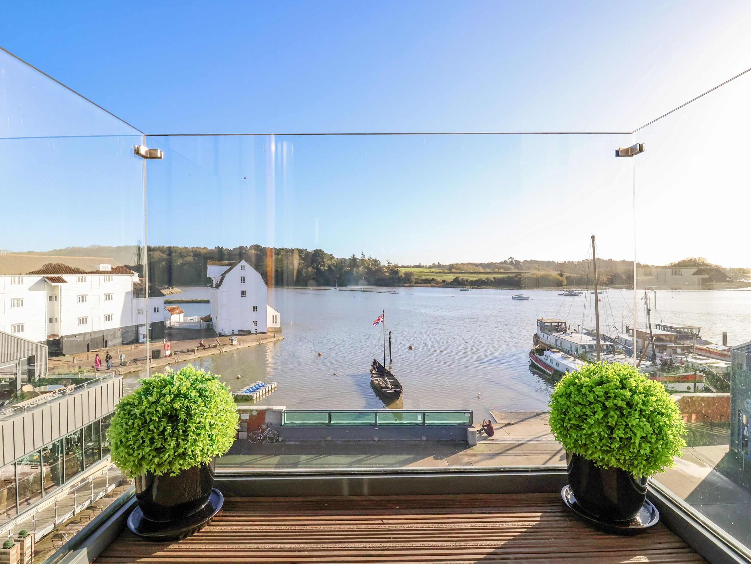 Un balcone con vista su un fiume tranquillo, imbarcazioni e un edificio bianco dall'altra parte dell'acqua.