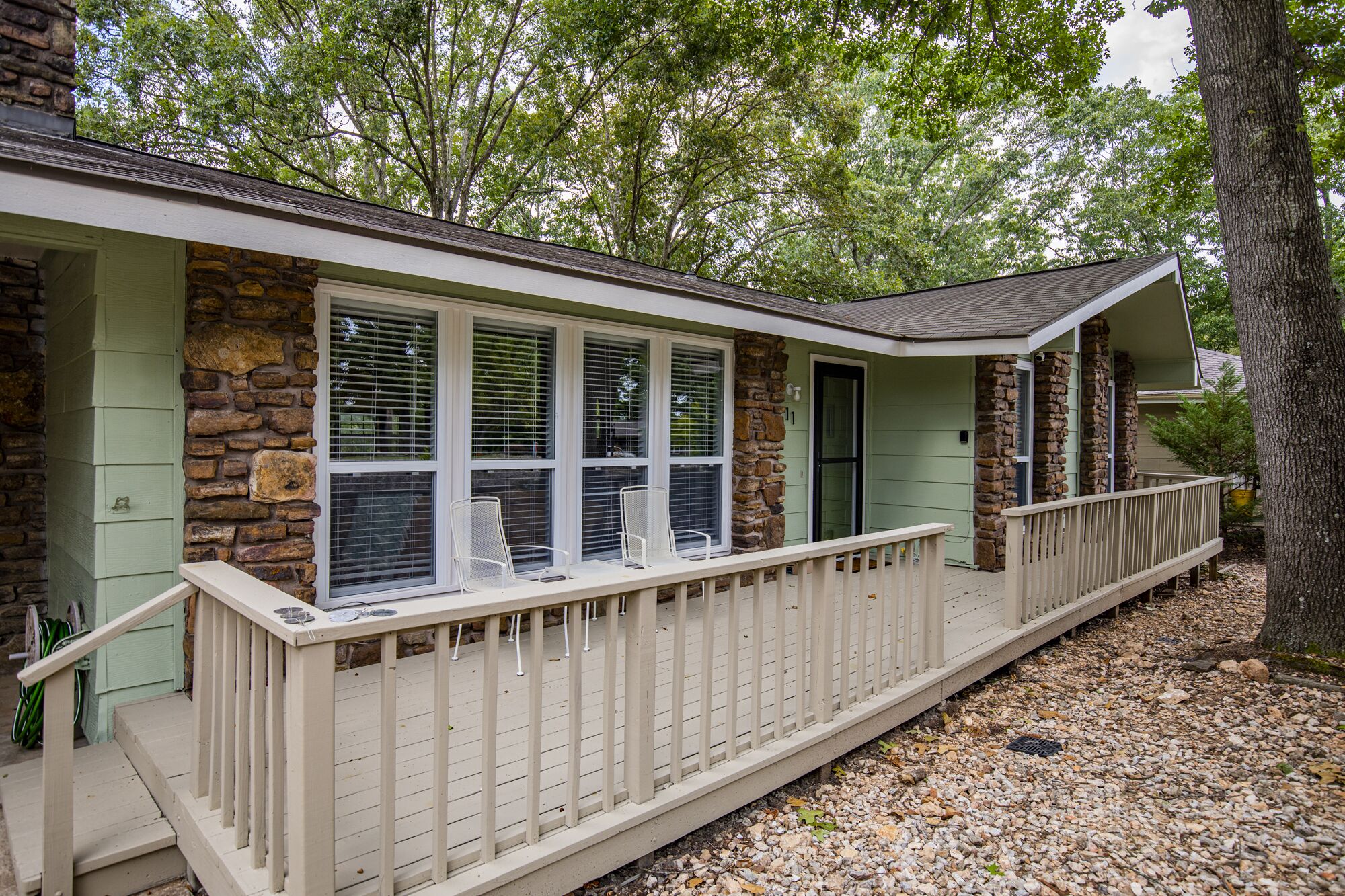 A house with a stone facade, a covered porch with a railing, and a door with a number '11' sign.