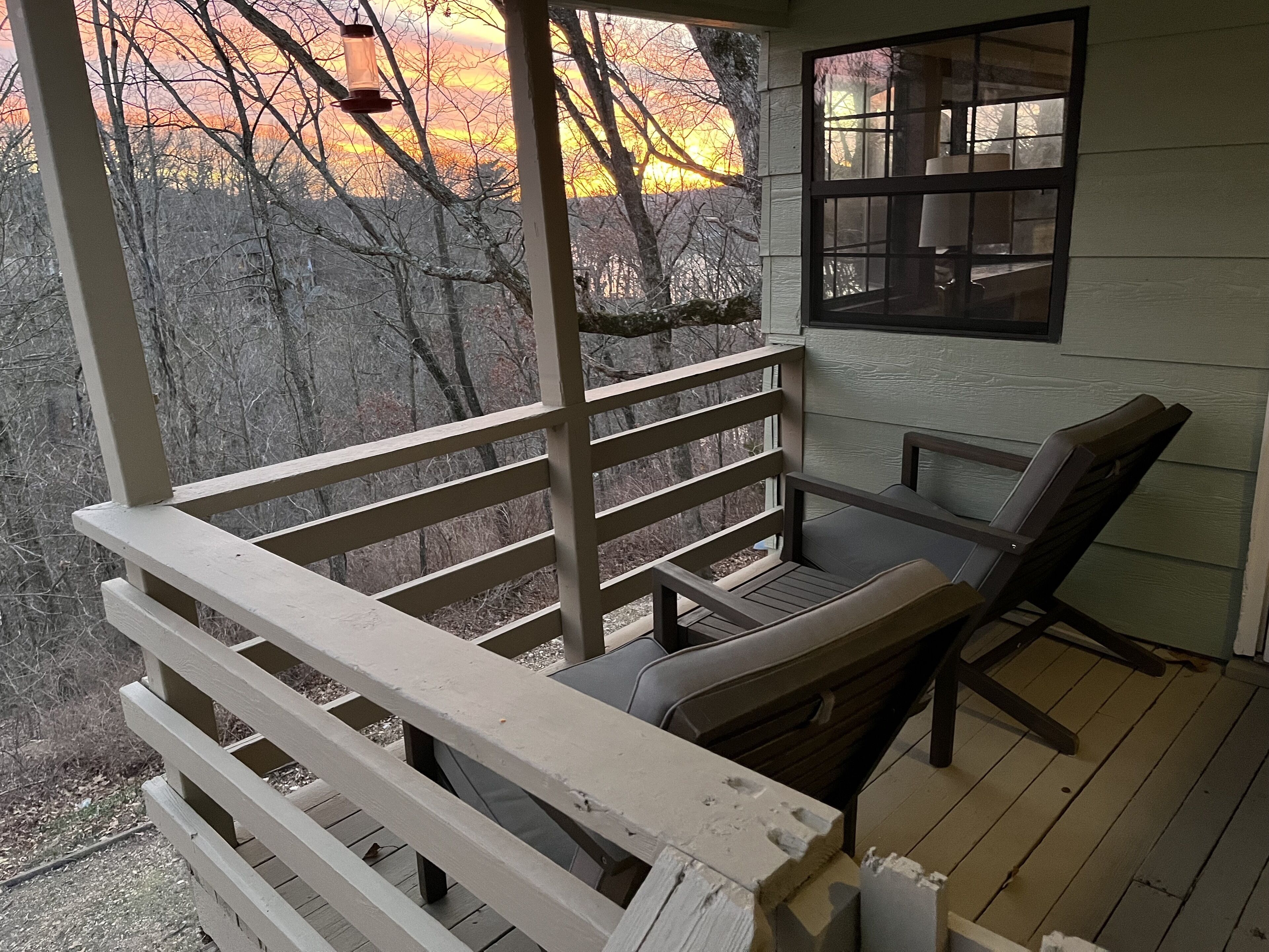 Une véranda avec un banc en bois et une table, donnant sur une zone boisée.
