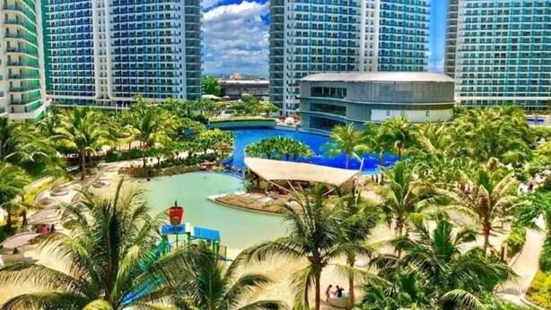 A resort with multiple high-rise buildings, a central swimming pool, and surrounding palm trees. - Cozy 1BR cityview with Balcony and near Airport (Paranquae)