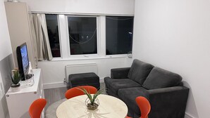 A modern living room with a grey sofa, orange chairs, a small round table, and a TV on a white cabinet.