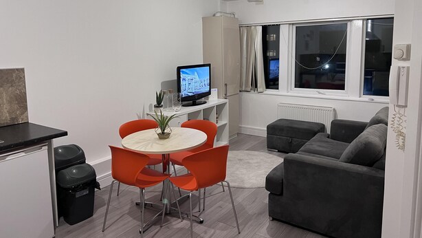 A modern living room with a dining area, grey sofa, and a TV on a stand.