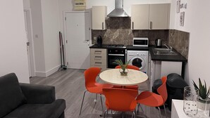 A compact kitchen with a microwave, stove, oven, and washing machine. There is a dining area with a round table and orange chairs.