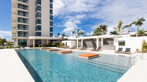 Una piscina con sillones de descanso, un edificio alto y palmeras.
