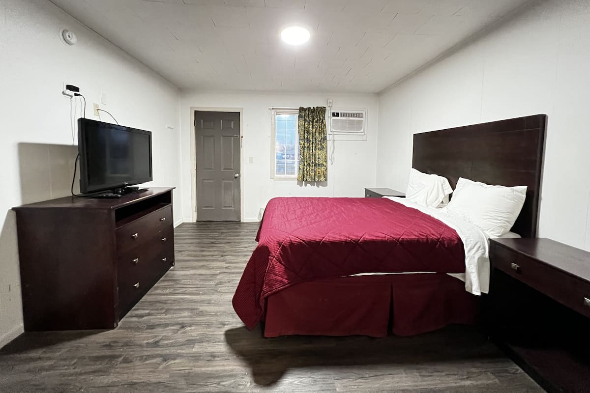 A bedroom with a bed, a dresser, a television, and an air conditioning unit.