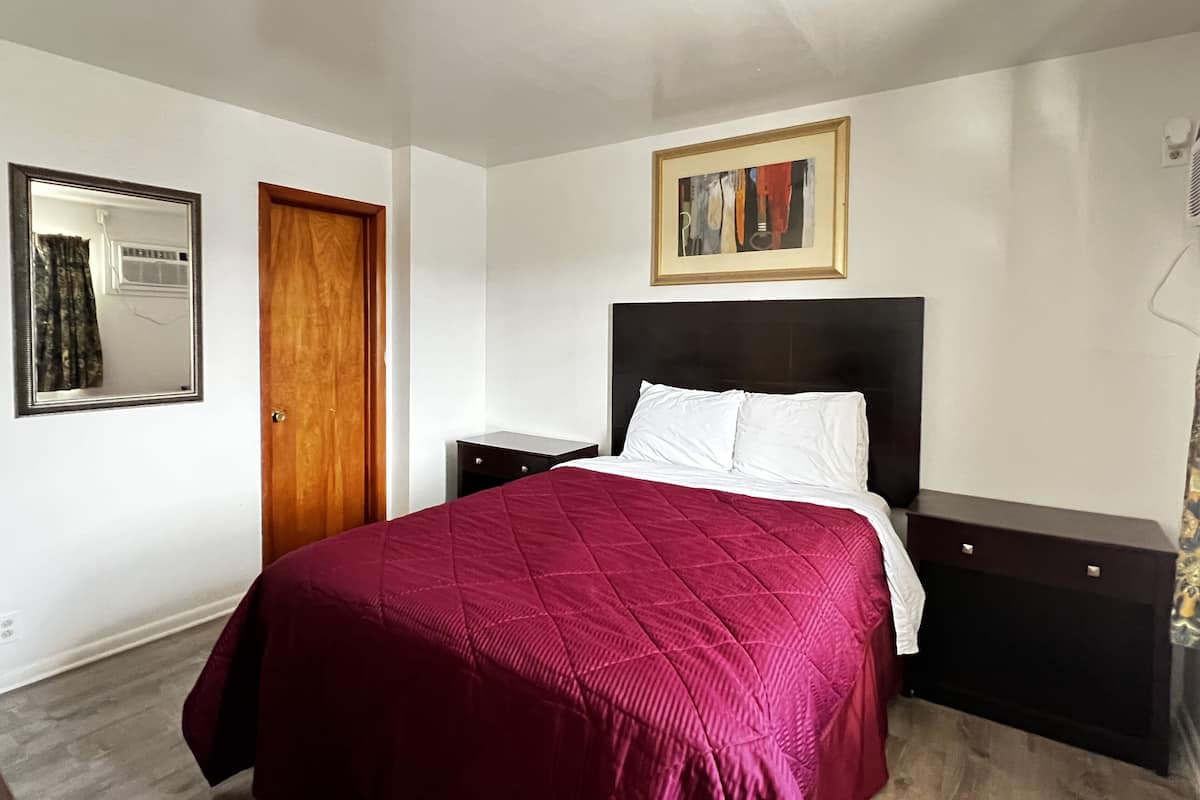 A bedroom with a bed, a nightstand, a dresser, a mirror, and a painting on the wall.