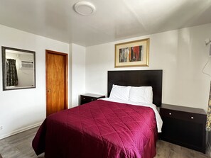 A bedroom with a bed, a nightstand, a dresser, a mirror, and a painting on the wall. - Family Inn (Watseka)