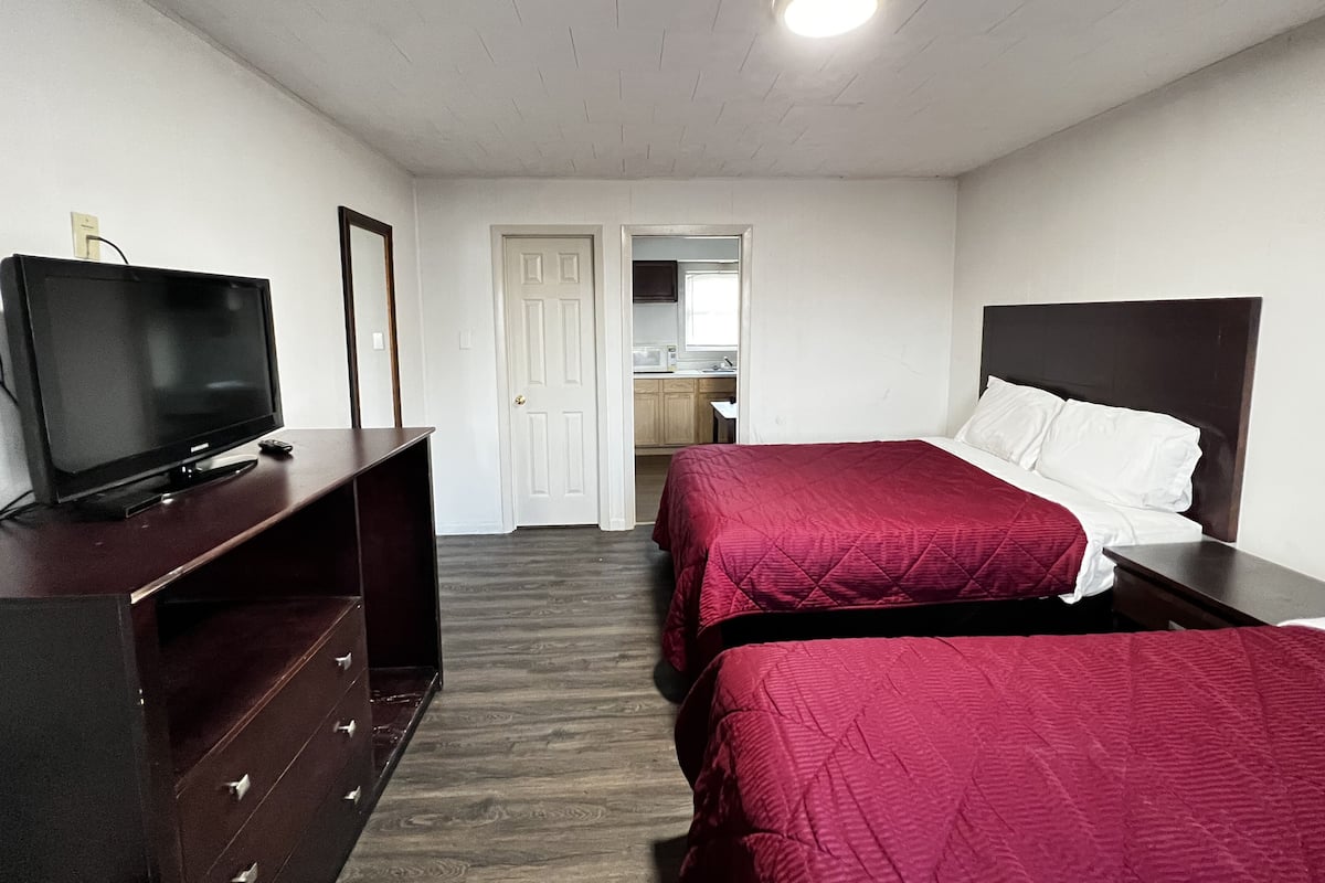 A hotel room with two beds, a TV on a dresser, and a door leading to a bathroom.