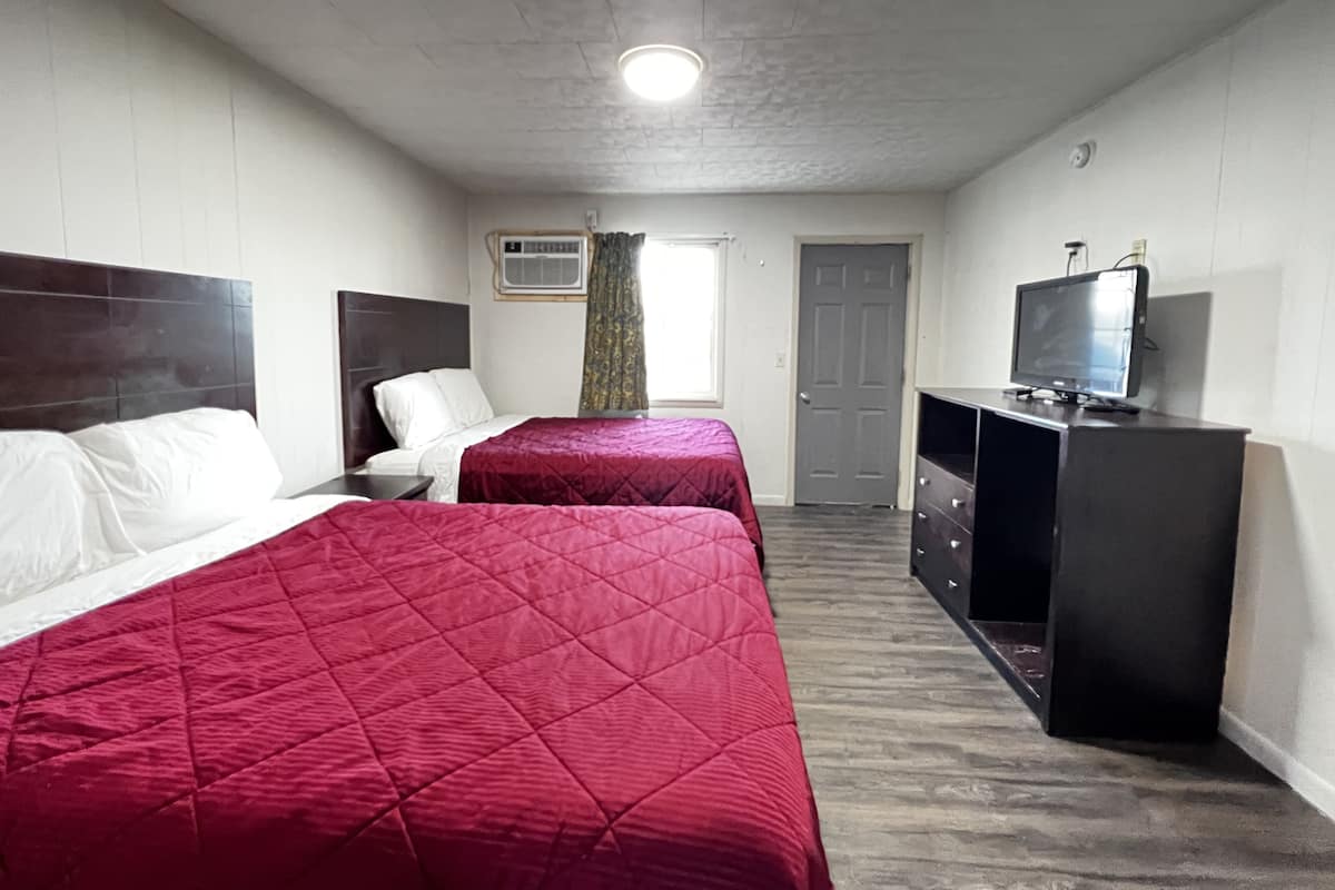 A hotel room with two beds, a TV, a dresser, and a door.