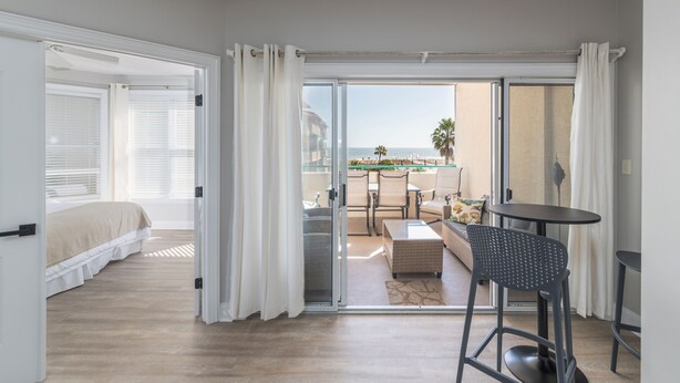Een hotelkamer met een bed, een balkon met tafel en stoelen, en uitzicht op het strand.