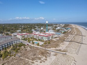 An aerial view of a coastal hotel with multiple buildings, a beach, and a lighthouse in the background. - Ocean Pearl with Oceanviews, On-site Pool (Tybee Island)