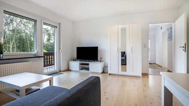 A modern living room with a flat-screen TV, a sofa, a dining table, and a sliding glass door leading to a balcony. - Apartment "Große" with Mountain View, Terrace & Wi-Fi (Osterode am Harz)