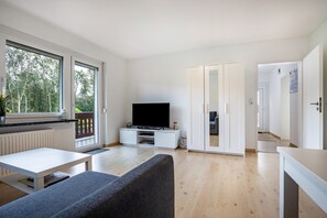 Una sala moderna con televisor de pantalla plana, sofá, mesa de comedor y puerta corrediza de vidrio que da a un balcón.