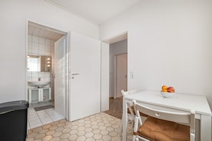 Um quarto com uma mesa branca, uma cadeira branca, uma almofada marrom, uma pia branca e um espelho com luzes.