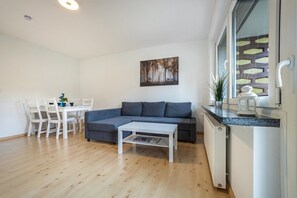 Uma sala de estar moderna com um sofá cinzento, uma mesa de centro branca e uma área de jantar com cadeiras brancas.