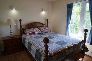 A bedroom with a wooden bed, a nightstand, a lamp, and a window with curtains.