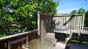 An outdoor deck with a glass-top table and metal chairs, a grill, and a wooden fence. - Great Location - North Rustico Ocean View (North Rustico)