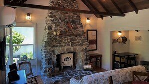 Une pièce chaleureuse avec une cheminée en pierre, des poutres apparentes et un coin repas comprenant une table et des chaises.