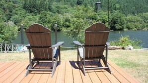 Deux fauteuils Adirondack sont placés face à un lac, avec une colline boisée en arrière-plan.