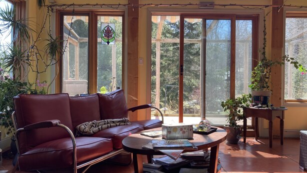 A sunlit room with a leather sofa, a small table with books, and large windows with a view of trees. - Secluded cottage on Seguin river with sauna and screened in porch (Seguin)