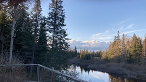 A wooden deck overlooking a calm lake with dense forest and mountains in the background. - Secluded cottage on Seguin river with sauna and screened in porch (Seguin)