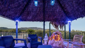 Un espacio al aire libre con mobiliario de mimbre, una escultura de piedra y una estructura de techo de paja.