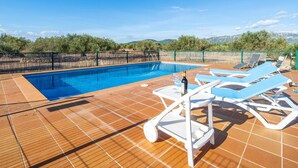 Una piscina con vistas a montañas, rodeada por un área cercada con sillones de descanso.