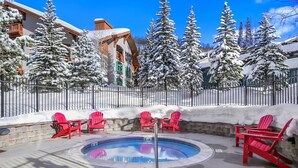 A snow-covered outdoor pool area with red Adirondack chairs, a pool, and snow-laden trees.