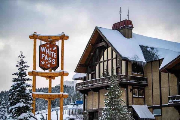 A wooden sign with "WHITE PASS" written on it, a building with a snow-covered roof, and snow-covered trees in the background.