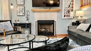 Ein Wohnzimmer mit Kamin, einer Couch, einem Couchtisch und einem Fernseher, der über dem Kamin angebracht ist.