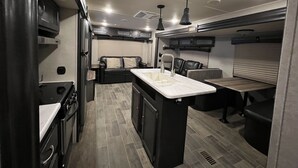 A compact RV kitchen with a central island, a built-in stove, and a dining area with a bench. - The Little Sweet Home (Spring Hill)