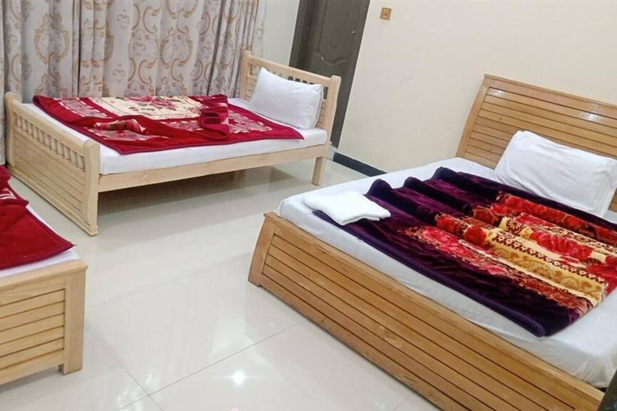Ein Hotelzimmer mit zwei hölzernen Betten, jeweils mit einer rot-weißen Bettdecke. Der Raum hat einen gefliesten Boden und eine Tür im Hintergrund.