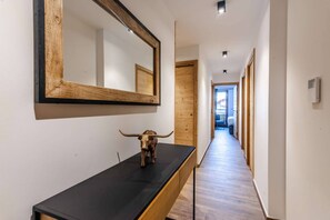 A hallway with a wooden floor, a black console table with a bull sculpture, and a large mirror on the wall. - Best location in Morzine, direct access to Avoriaz (MORZINE)