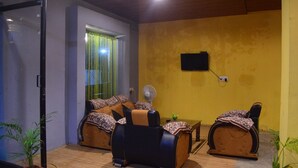 Um quarto com duas cadeiras de massagem, uma mesinha, um ventilador e uma televisão fixada na parede.