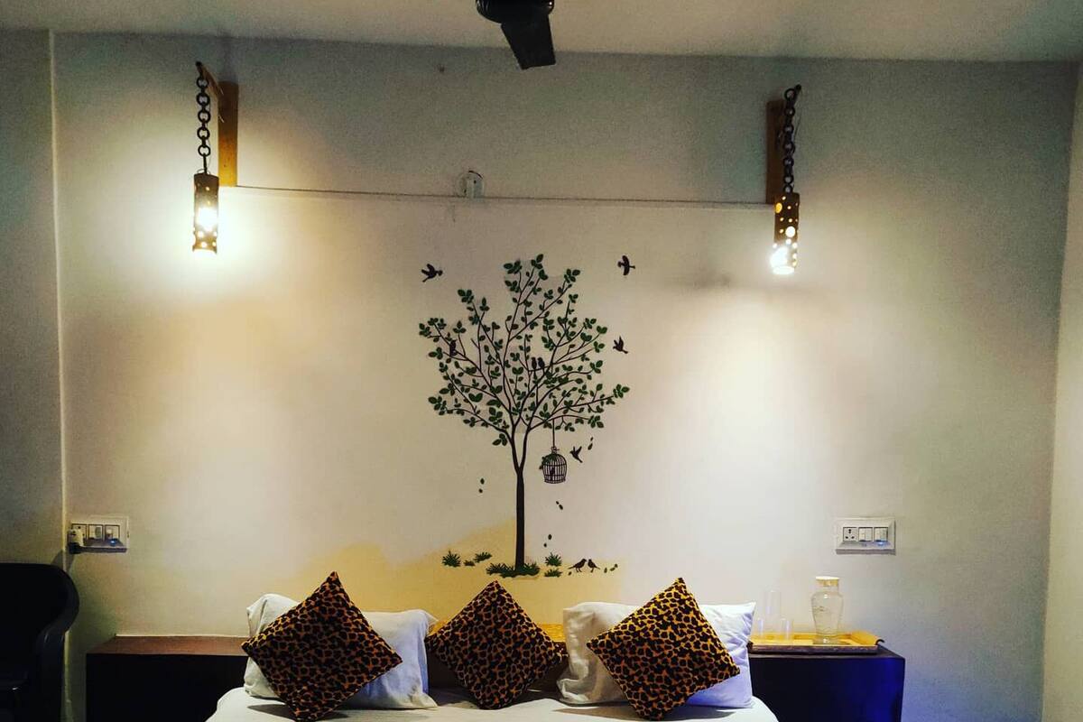 Quarto com cama, almofadas de estampa de leopardo, painel de parede com tema de árvore e luminárias de cabeceira.