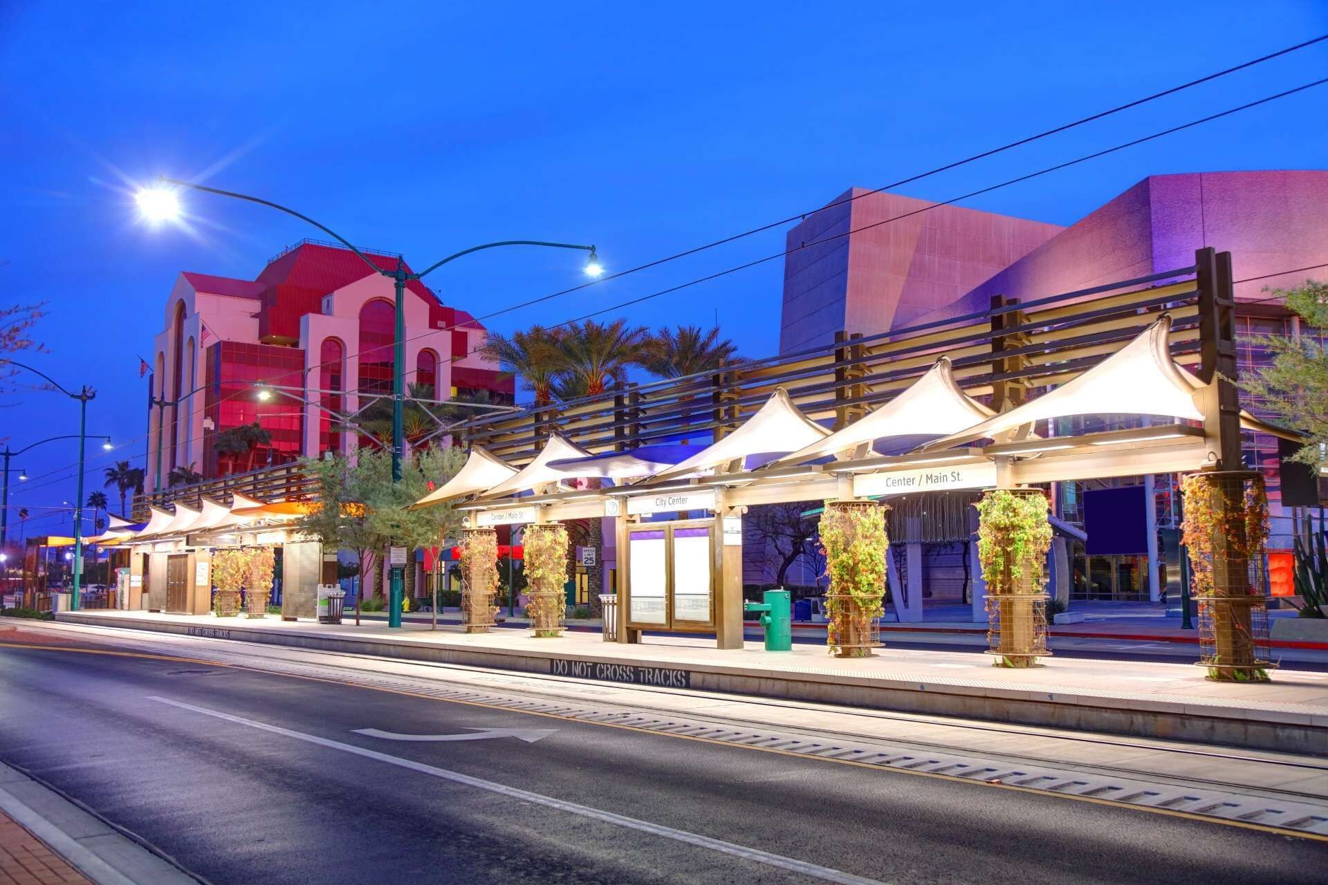 A street view with a tram station, a building with a red facade, and a clear sky.