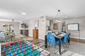 A spacious living room with a foosball table, a dining area with blue chairs, and a kitchen in the background. - 4BR Gilbert Home | Dog Friendly | Ping Pong & Foosball | Large backyard | Downtown Less Than 1 Mile (Gilbert)