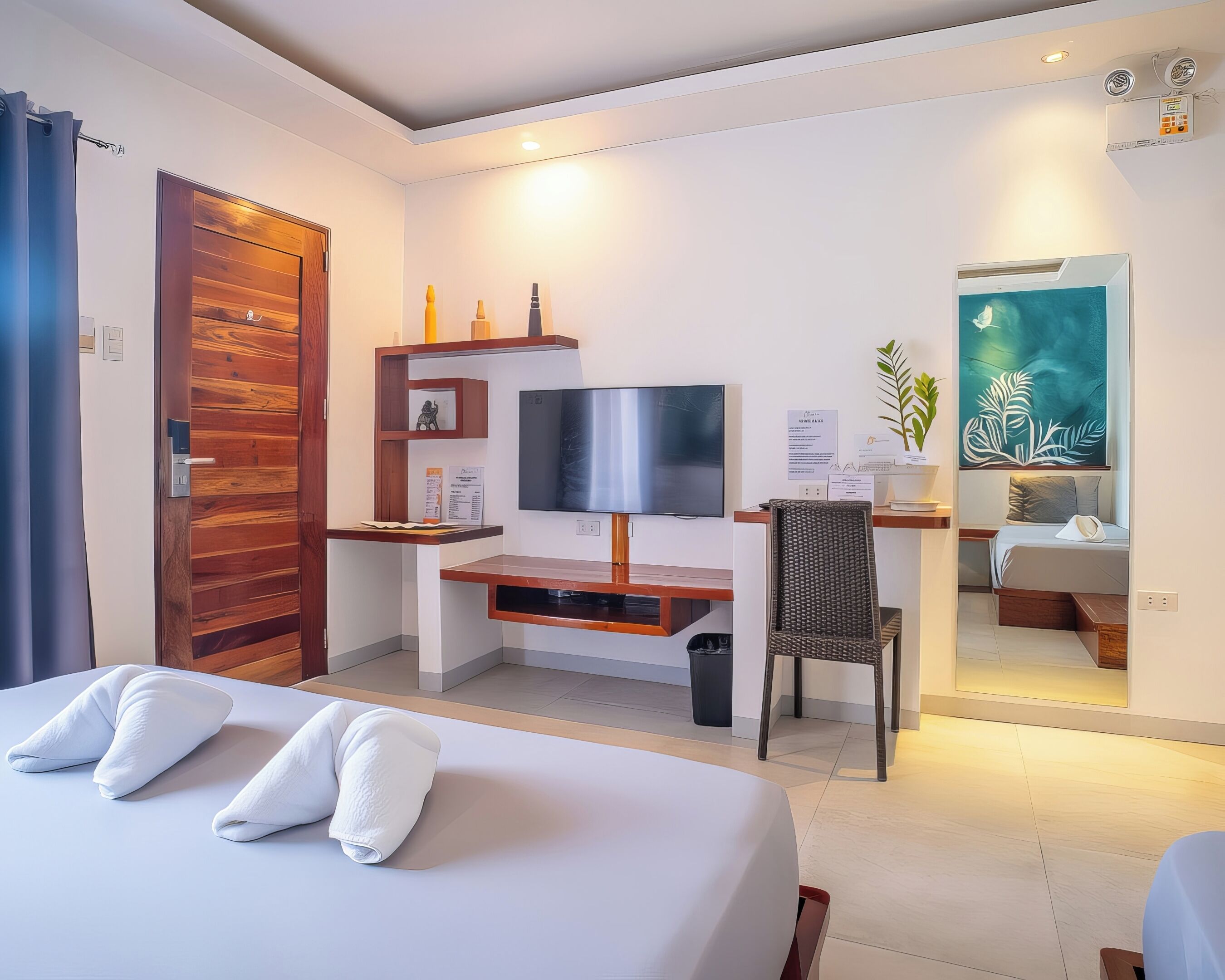 Een hotelkamer met een bed, een bureau met een televisie, een stoel, een spiegel en een plant.