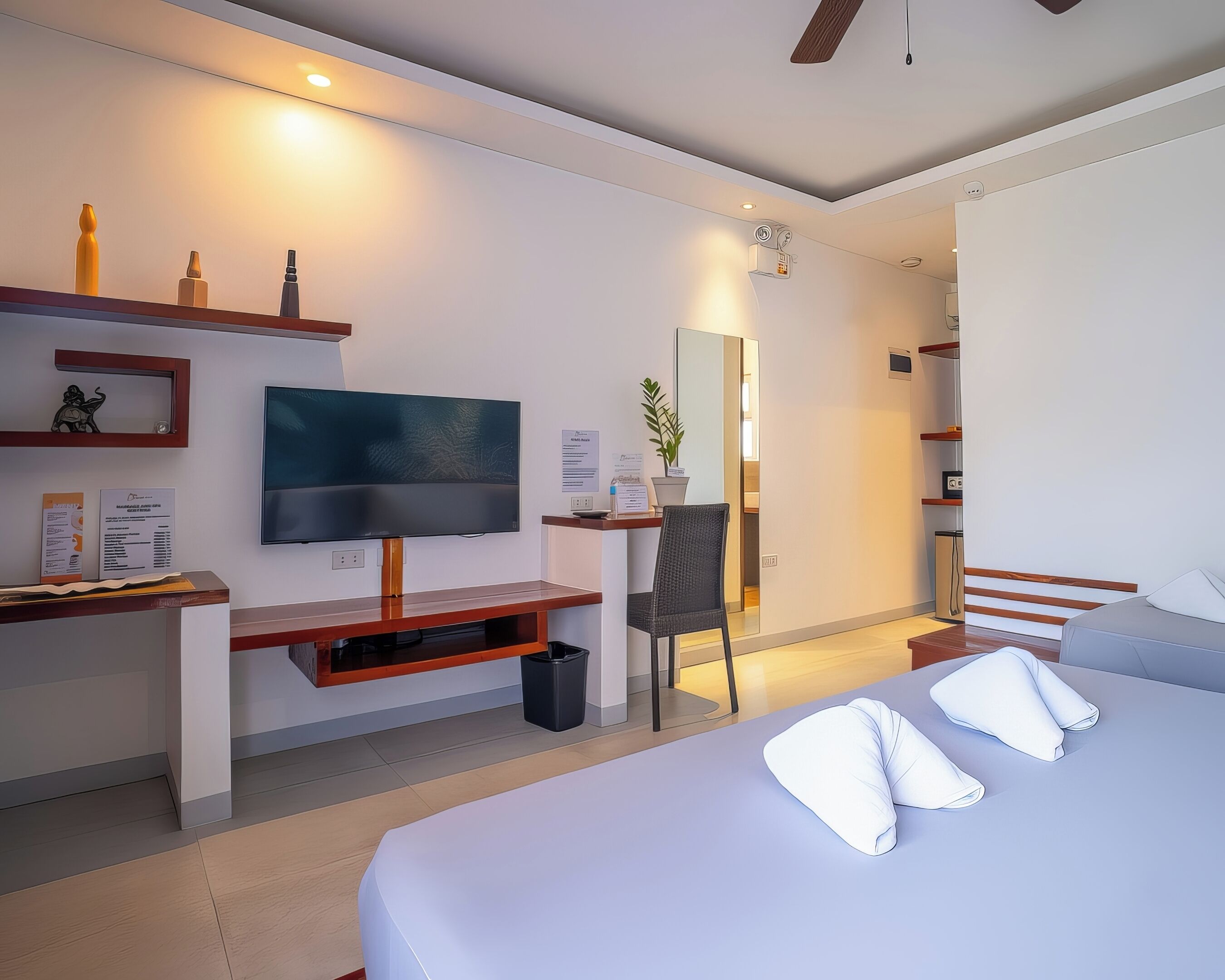 A modern hotel room with a large bed, a TV, a desk, and a mirror.