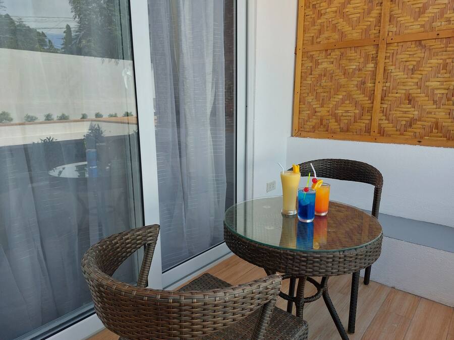 Mesa de vidro com cadeiras de vime numa varanda com vista para um edifício e um painel de parede trançado.