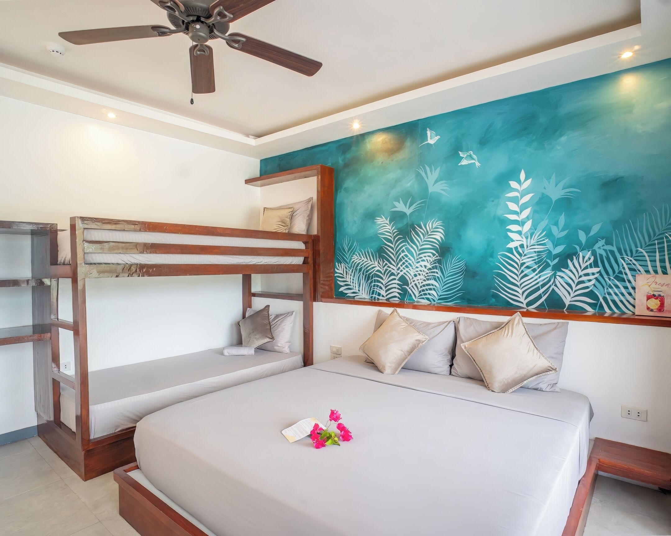 A bunk bed room with a ceiling fan, a teal wall mural, and a bed with pillows.