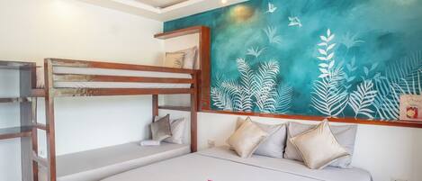 Habitación con literas, ventilador de techo, un mural en la pared color aguamarina y una cama con almohadas.